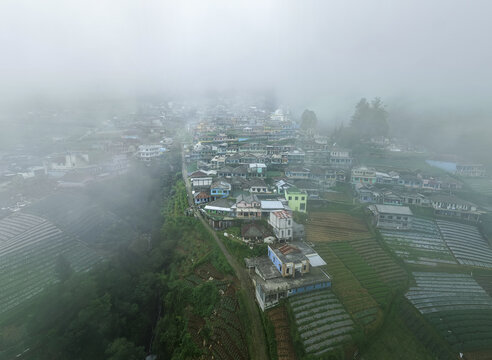 Aerial view of Nepal Van Java village with colorful houses on a steep slope, terraced fields, and thick morning mist in Kecamatan Kaliangkrik, Jawa Tengah, Indonesia.