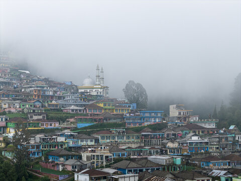 Aerial view of Nepal Van Java village with colorful houses and a prominent mosque nestled on the misty slopes of Mount Sumbing in Kecamatan Kaliangkrik, Jawa Tengah, Indonesia.