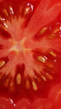 Macro view of a ripe, juicy tomato slice, showcasing its vibrant red pulp and numerous seeds in stunning detail.