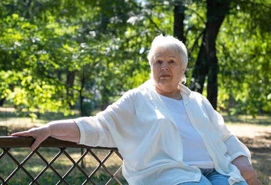 Senior woman sitting on bench in city park. Retired elderly lady outdoors on sunny summer day