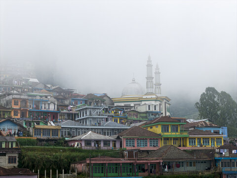 Aerial view of Nepal Van Java featuring colorful houses on a steep hillside and a prominent mosque under thick fog in Kecamatan Kaliangkrik, Jawa Tengah, Indonesia.