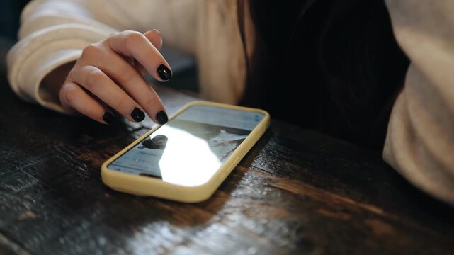 A girl sits on the bar counter and flips through the pages on her phone with her fingers. Close-up shooting
