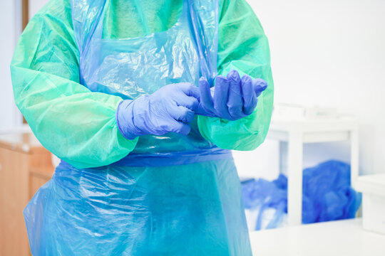 A medical worker puts on blue nitrile protective gloves while wearing a green gown and plastic apron in a clinic to signify rigorous hygiene standards for patient safety and health