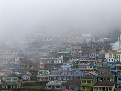 Aerial view of Nepal Van Java village with colorful houses on a hillside partially covered by thick fog in Kecamatan Kaliangkrik, Jawa Tengah, Indonesia.
