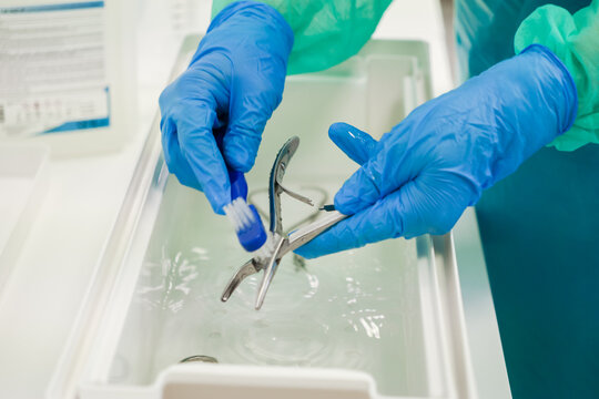 A dedicated medical professional cleans surgical instruments in a sterile liquid basin using a small brush to ensure high hygiene and safety standards in a modern clinical setting
