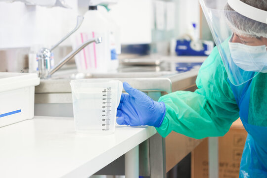 Medical professional wearing protective gear holds a plastic beaker in a sterile laboratory setting, demonstrating clinical precision during a controlled scientific research procedure