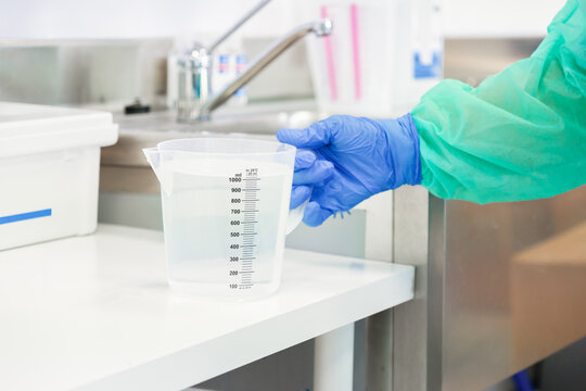 Gloved hand holding a clear plastic measuring jug with liquid in a professional laboratory, reflecting sterile scientific procedures and accurate chemical preparation in a research site