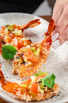 Hand picking crispy breaded shrimp appetizer with fresh salsa on restaurant plate close up