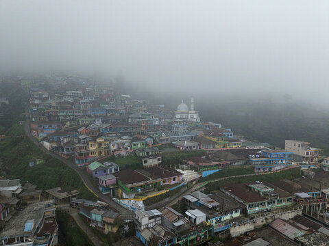 Aerial view of Nepal Van Java village with colorful houses and a mosque dome partially hidden by thick morning fog on Mount Sumbing Kecamatan Kaliangkrik, Jawa Tengah, Indonesia.