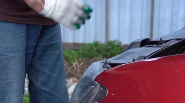 A Close-Up of a Car's Hood Being Inspected with Careful Attention by a Person Wearing Protective Gloves in a Backyard Setting