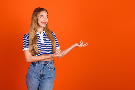 Charming young woman presenting with cheerful expression on orange background in trendy casual style and striped shirt
