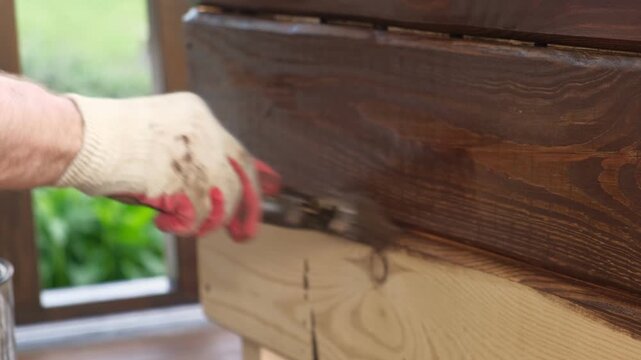 Brown oil for protection of wood by staining. Painting fence for protecting and pests. Woodworker applying finish to pine board box. Repairman varnishing with brush wooden fencing wall plank surface.