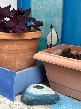 Decorative pots and painted stones are placed on a small table in a garden area during daytime hours in a colorful outdoor setting