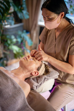 Focused lady masseuse making anti-aging lifting massage for female client resting on spa table, cosmetologist massaging woman patient forehead gently gliding on skin, wellbeing and self love therapy