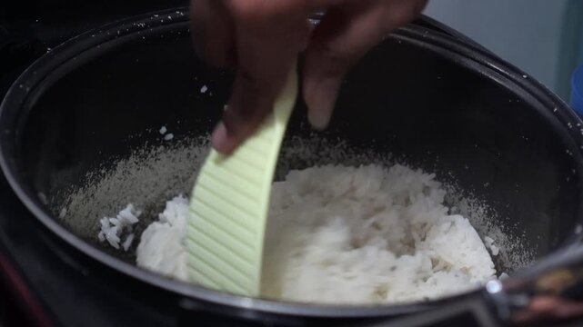 Close-up of person stirring cooked white rice in an old peeling non-stick pot.