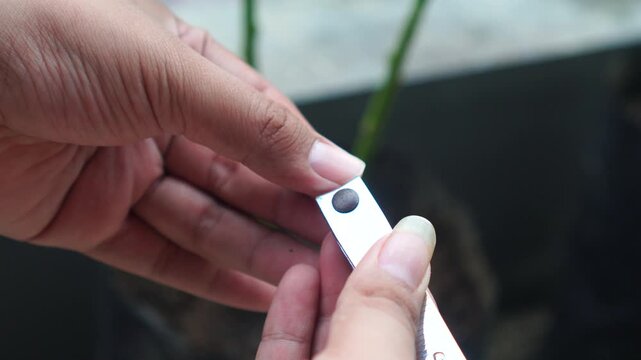 Close-up of a person cutting fingernails with a metal clipper in an outdoor setting.
