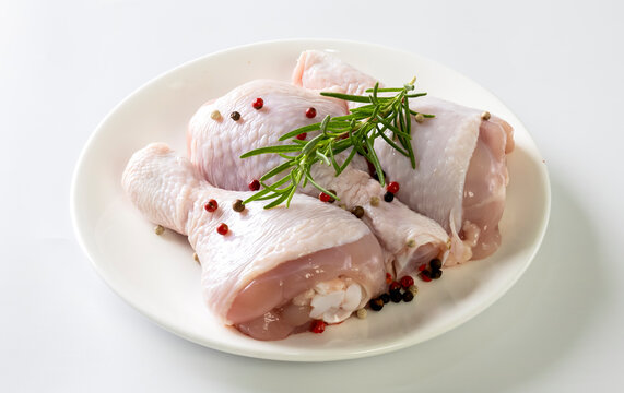 Raw chicken drumsticks with spices on plate isolated on white