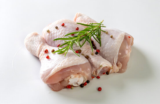 Raw chicken drumsticks with spices on plate isolated on white