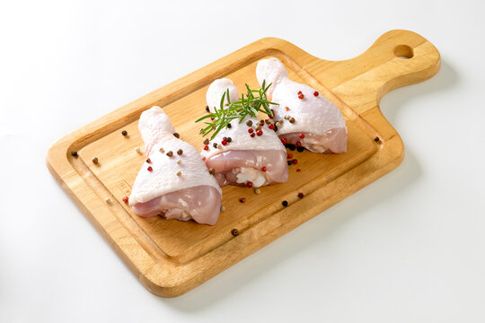 Seasoned raw chicken drumsticks on a cutting board, placed separately on a white background.