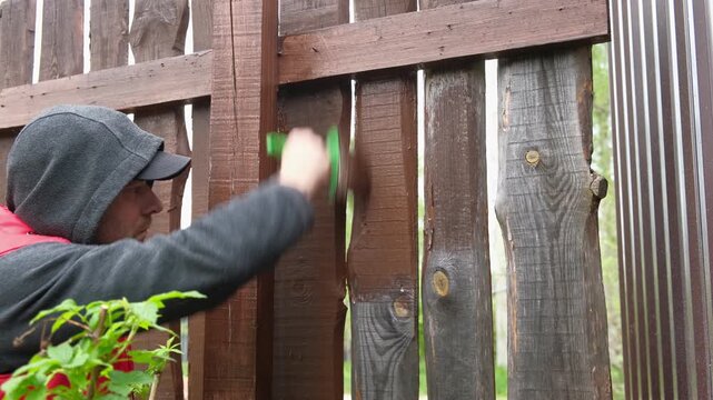 Brown oil for protection of wood by staining. Painting fence for protecting and pests. Woodworker applying finish to pine deck board. Repairman varnishing with brush wooden fencing wall plank surface.