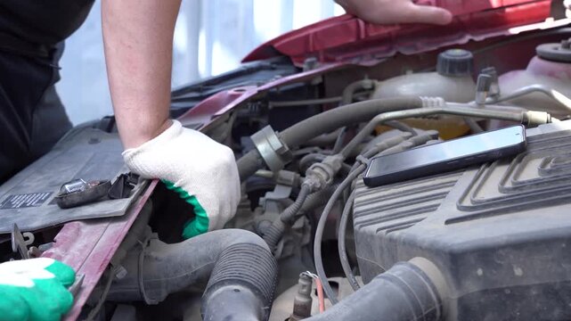 A Mechanic's Precision: An Expert Technician Diagnosing Issues Under the Hood with Attention to Detail While Using a Mobile Device for Assistance