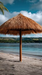 Fototapeta premium View of a beach with a large thatched umbrella and a turquoise ocean under a partly cloudy sky with distant mountains and small boats