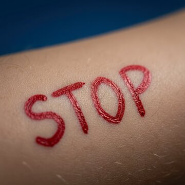 Close-up of a red 'STOP' tattoo on a forearm against a blue background