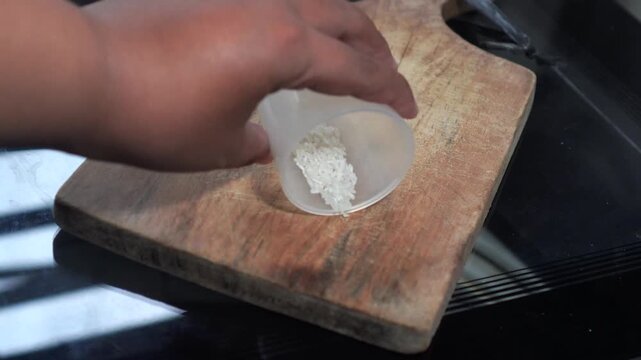 Close-up of hand pouring and spreading a small amount of rice on wood.