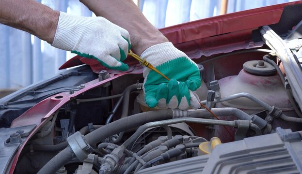 Hands in Gloves Performing an Oil Dipstick Check Under the Hood of a Vehicle to Ensure Proper Engine Lubrication and Maintenance