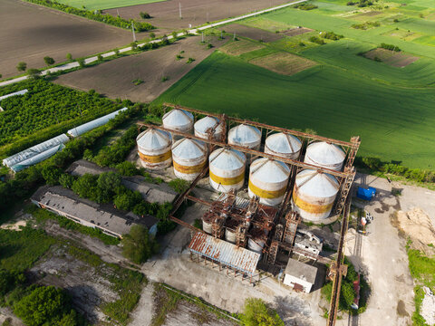 Aerial view of large grain silos and industrial agricultural buildings surrounded by green fields and tilled land in Balchik, Dobrich Province, Bulgaria.