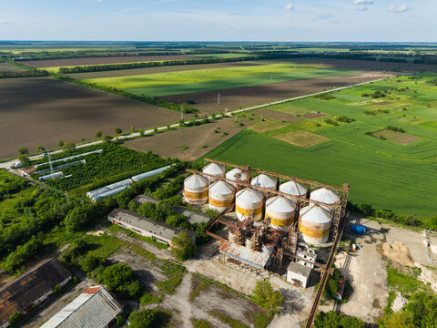 Aerial view of industrial grain silos and vast agricultural fields under a clear blue sky in Balchik, Dobrich Province, Bulgaria.