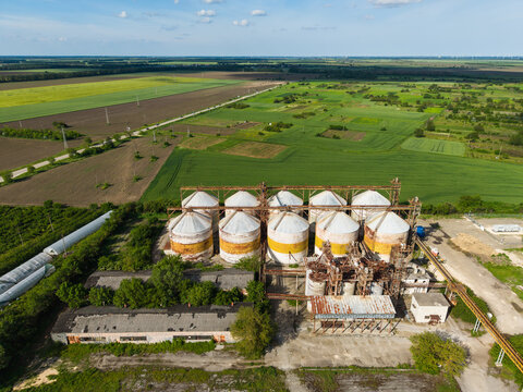 Aerial view of industrial grain silos and storage facility surrounded by vast green agricultural fields and rural landscape in Balchik, Dobrich Province, Bulgaria.