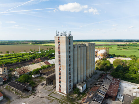 Aerial view of a tall concrete grain elevator with telecommunication antennas on top surrounded by old industrial buildings and green fields Balchik, Dobrich Province, Bulgaria.
