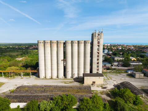 Aerial view of large concrete grain silos and industrial buildings surrounded by green trees under a blue sky Balchik, Dobrich Province, Bulgaria.