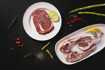 Raw beef steak and lamb chops with asparagus, citrus and herbs on dark background © TranVan
