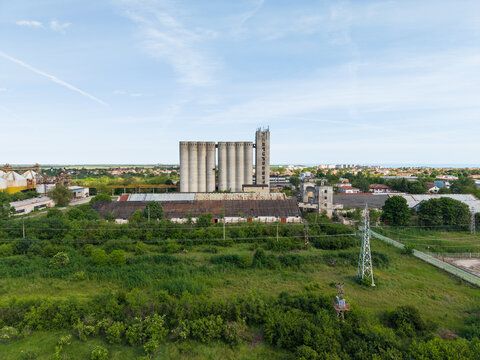 Aerial view of large concrete grain silos and industrial warehouses surrounded by lush green vegetation and power lines Balchik, Dobrich Province, Bulgaria.