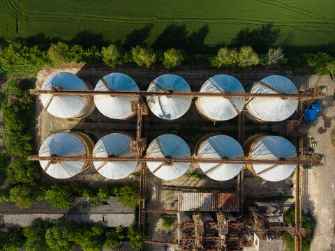Aerial view of industrial grain silos with white conical roofs and metal structures surrounded by green fields and trees in Balchik, Dobrich Province, Bulgaria.
