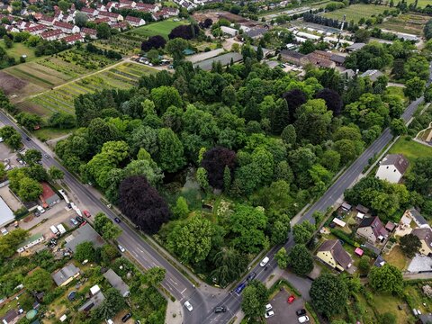 Aerial view of the lush Spath-Arboretum featuring dense green trees and a small pond surrounded by residential houses and streets in Berlin, Berlin, Germany.