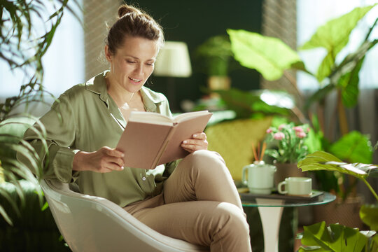 Seated in a modern white chair, a woman enjoys a quiet moment of reading amidst vibrant indoor plants and soft natural light.