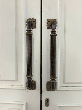 Antique brass door handles on white wooden doors of a historic manor house. Traditional architecture details and local lore tourism asset