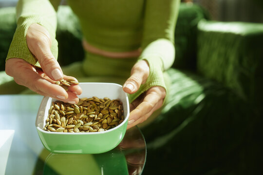Close-up of a person in athletic wear holding a bowl of raw pumpkin seeds, highlighting a mindful and nutritious choice for clean eating.