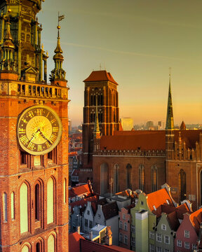 Aerial view of the Main Town Hall clock tower and St. Mary's Church with historic rooftops under a golden sunset in Gdansk, Pomeranian Voivodeship, Poland.
