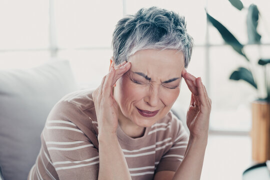 Senior woman holding her temples in pain from a headache or migraine while sitting at home