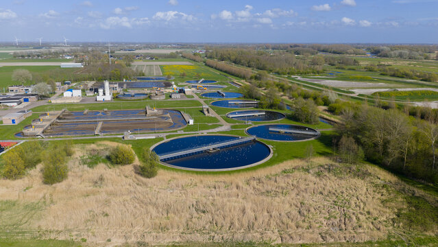 Aerial view of RWZI Geestmerambacht wastewater treatment plant featuring circular settling tanks and aeration basins surrounded by green fields and trees Warmenhuizen, Noord-Holland, Netherlands.