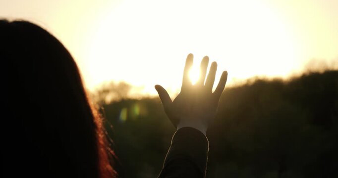 Female silhouette touching sunlight during sunset outdoors. Concept of connection with nature and harmony with environment. Silhouette of woman reaching hand towards sunset. Girl expresses hope