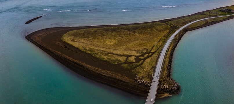 Aerial view of the Olfusa river estuary featuring a coastal road and bridge crossing black sand beaches and turquoise waters in Sveitarfelagid Arborg, Iceland.