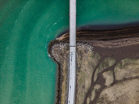 Aerial view of the Olfusa river estuary featuring a bridge crossing turquoise water and dark volcanic sand banks Sveitarfelagid Arborg, Iceland.