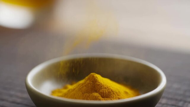 Slow motion shot of yellow turmeric powder being poured into a ceramic bowl on a wooden surface