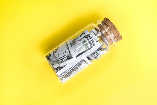Glass jar with rolled US dollar bills on yellow background