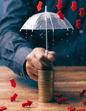 Market downturn hedge protection concept hand holding umbrella over coins business environment financial security strategy